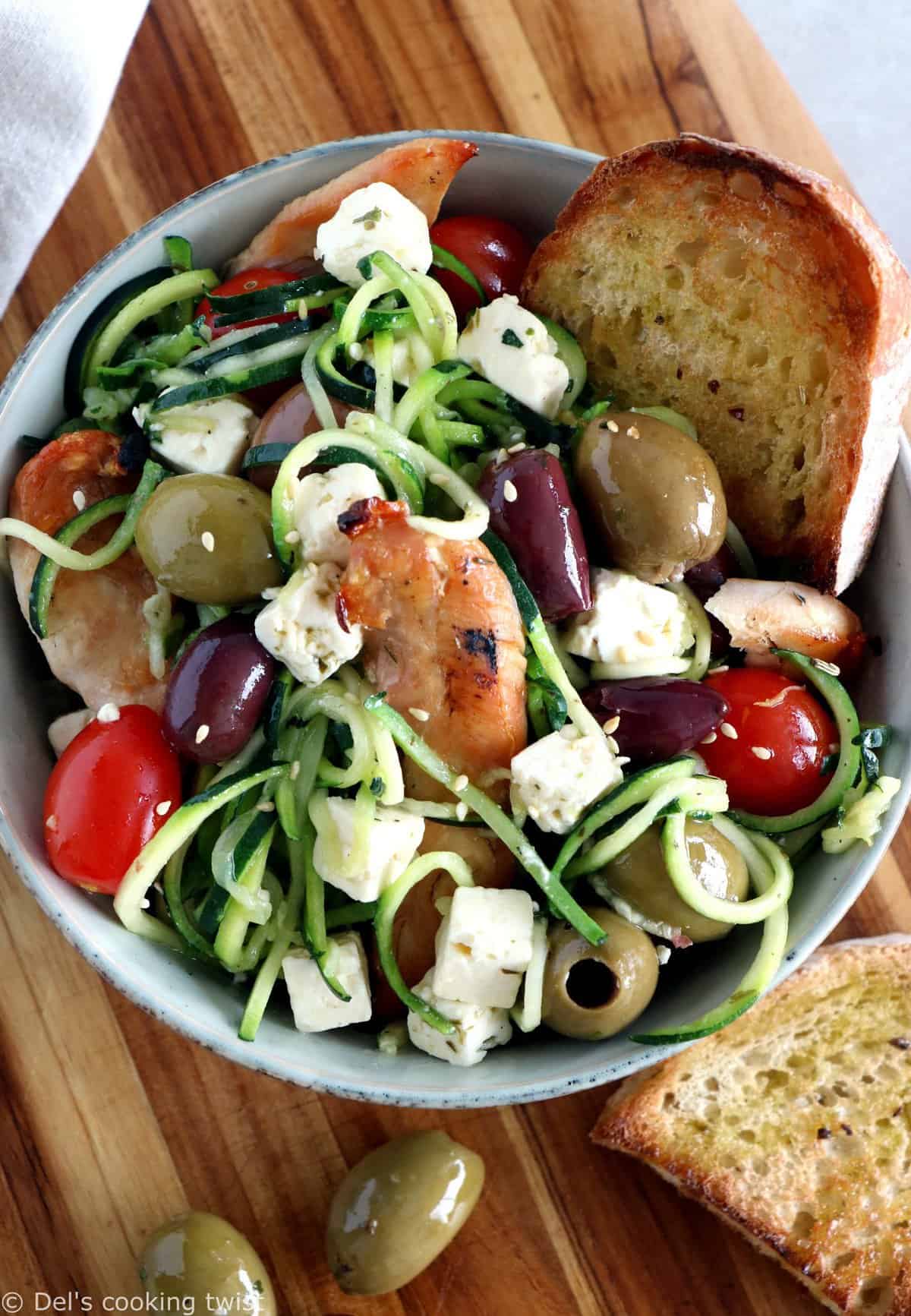 L'été s'invite dans notre assiette avec cette salade grecque de poulet aux spaghettis de courgettes et à la feta. Réalisée avec des courgettes coupées sous forme de spaghettis (zoodles), cette salade tiède est savoureuse, équilibrée, et réalisée sans gluten. 