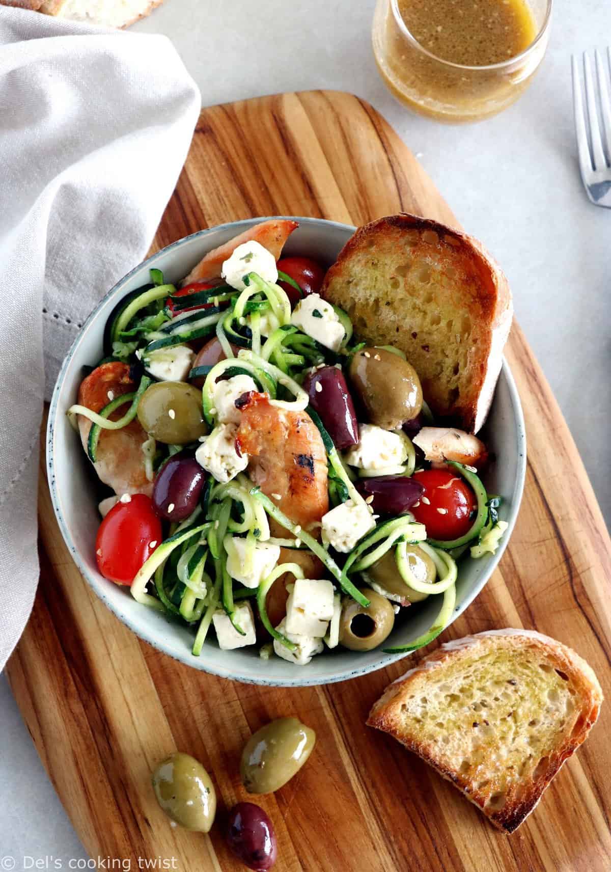 L'été s'invite dans notre assiette avec cette salade grecque de poulet aux spaghettis de courgettes et à la feta. Réalisée avec des courgettes coupées sous forme de spaghettis (zoodles), cette salade tiède est savoureuse, équilibrée, et réalisée sans gluten. 