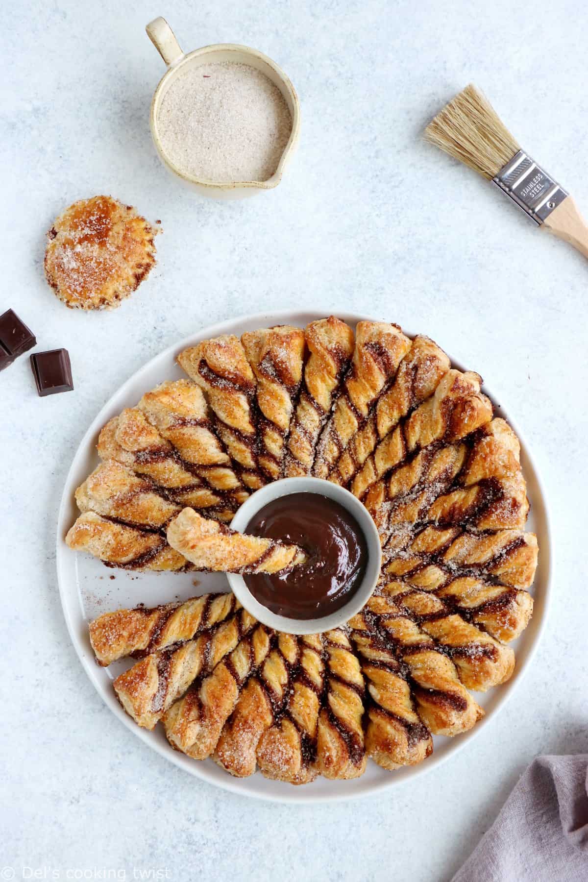 Vous ne résisterez pas à cette tarte soleil façon churros. Déchirez les torsades de pâte feuilletée recouvertes d'un mélange sucre-cannelle, trempez-les dans la sauce au chocolat chaud et dévorez sans plus attendre.