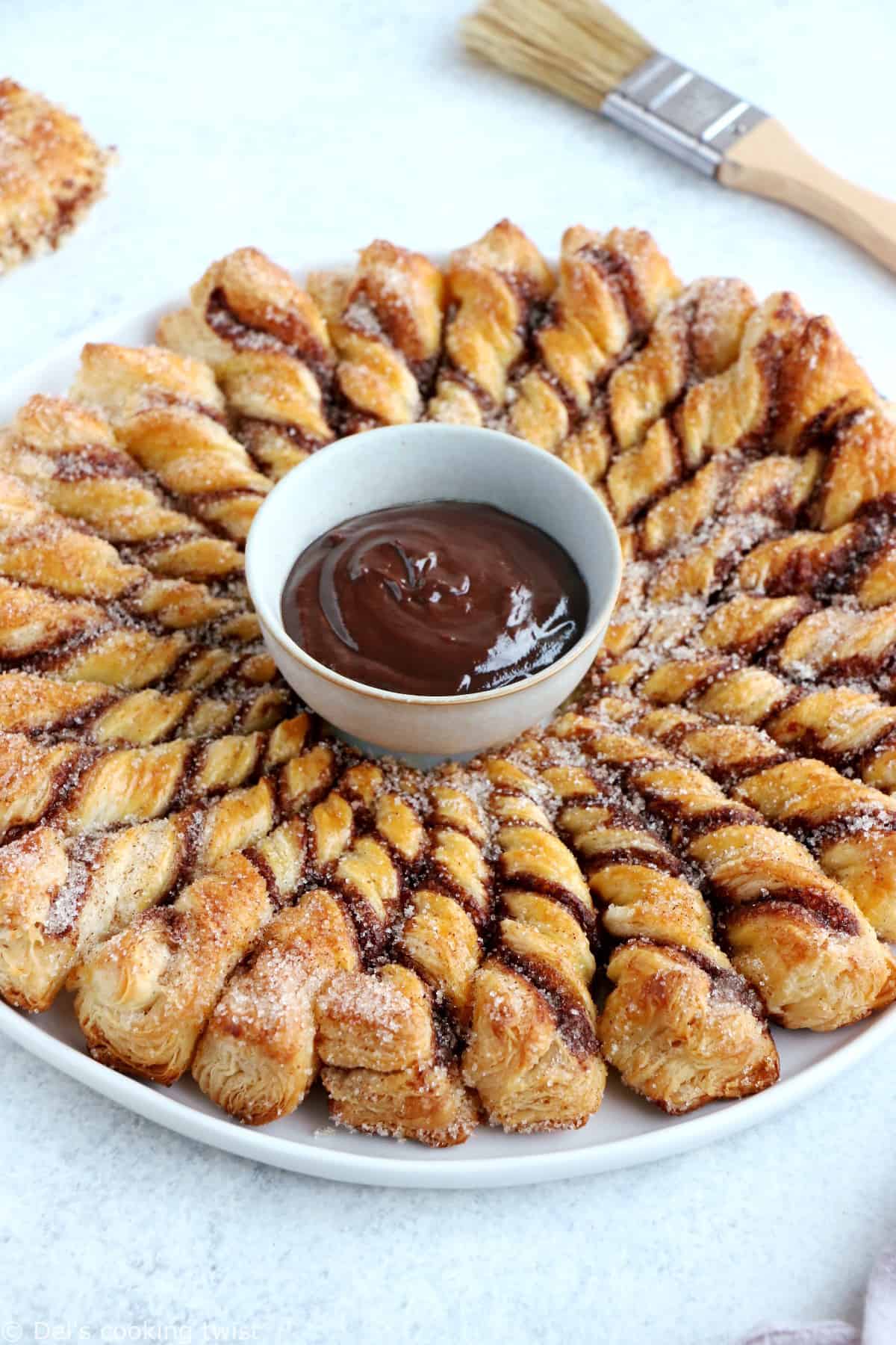 Vous ne résisterez pas à cette tarte soleil façon churros. Déchirez les torsades de pâte feuilletée recouvertes d'un mélange sucre-cannelle, trempez-les dans la sauce au chocolat chaud et dévorez sans plus attendre.