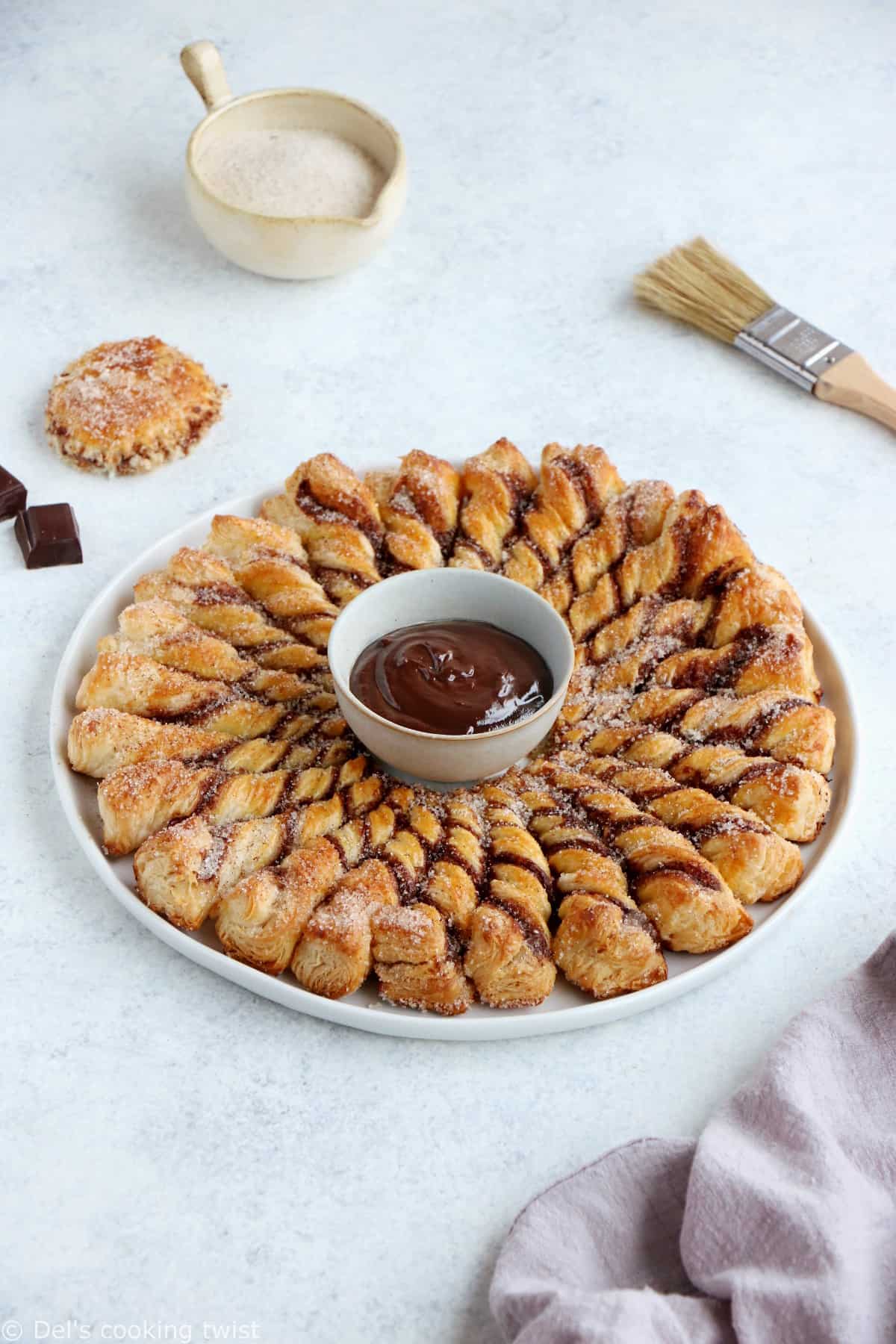 Vous ne résisterez pas à cette tarte soleil façon churros. Déchirez les torsades de pâte feuilletée recouvertes d'un mélange sucre-cannelle, trempez-les dans la sauce au chocolat chaud et dévorez sans plus attendre.