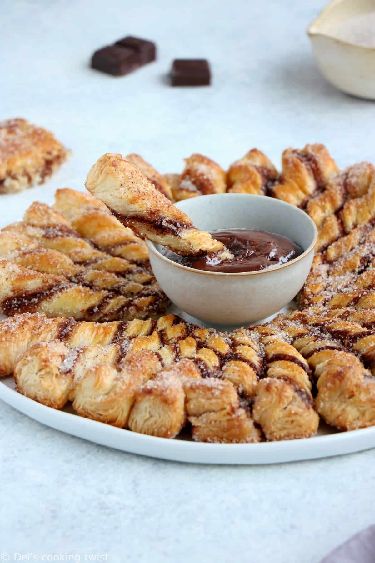 Vous ne résisterez pas à cette tarte soleil façon churros. Déchirez les torsades de pâte feuilletée recouvertes d'un mélange sucre-cannelle, trempez-les dans la sauce au chocolat chaud et dévorez sans plus attendre.