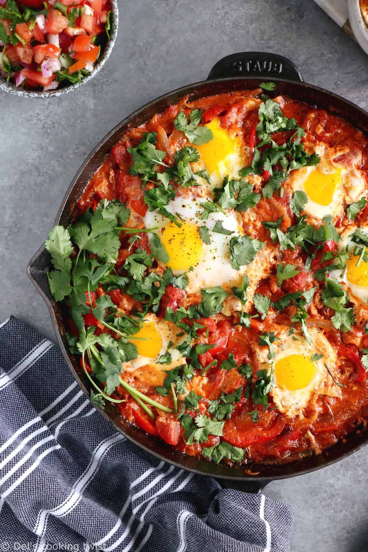 Shakshuka with Feta Cheese is a simple dish consisting of poached eggs in a simmering tomato sauce with feta and spices, traditionally served in a cast iron skillet.