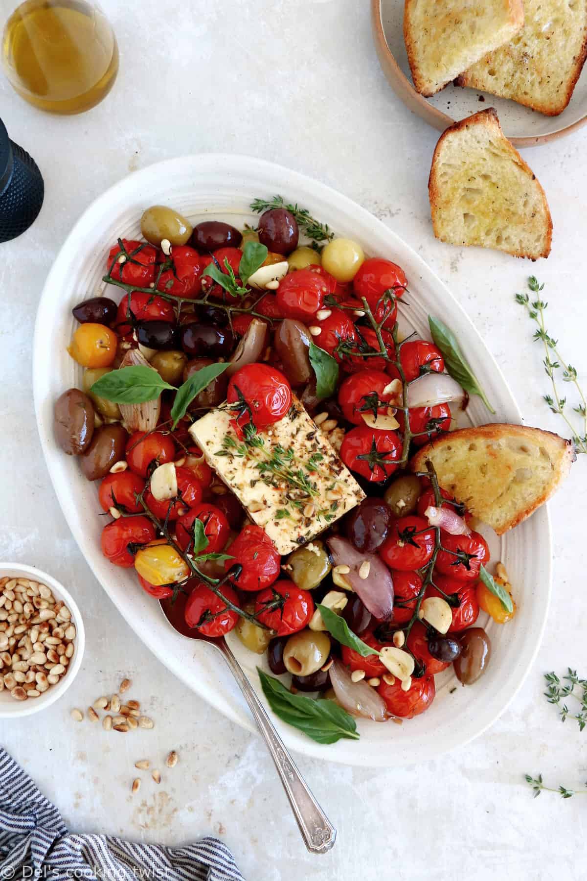 Découvrez ce plat de "baked feta", qui consiste en de la feta rôtie au four avec des tomates cerises confites et des olives marinées dans un mélange d'huile d'olive et d'herbes.