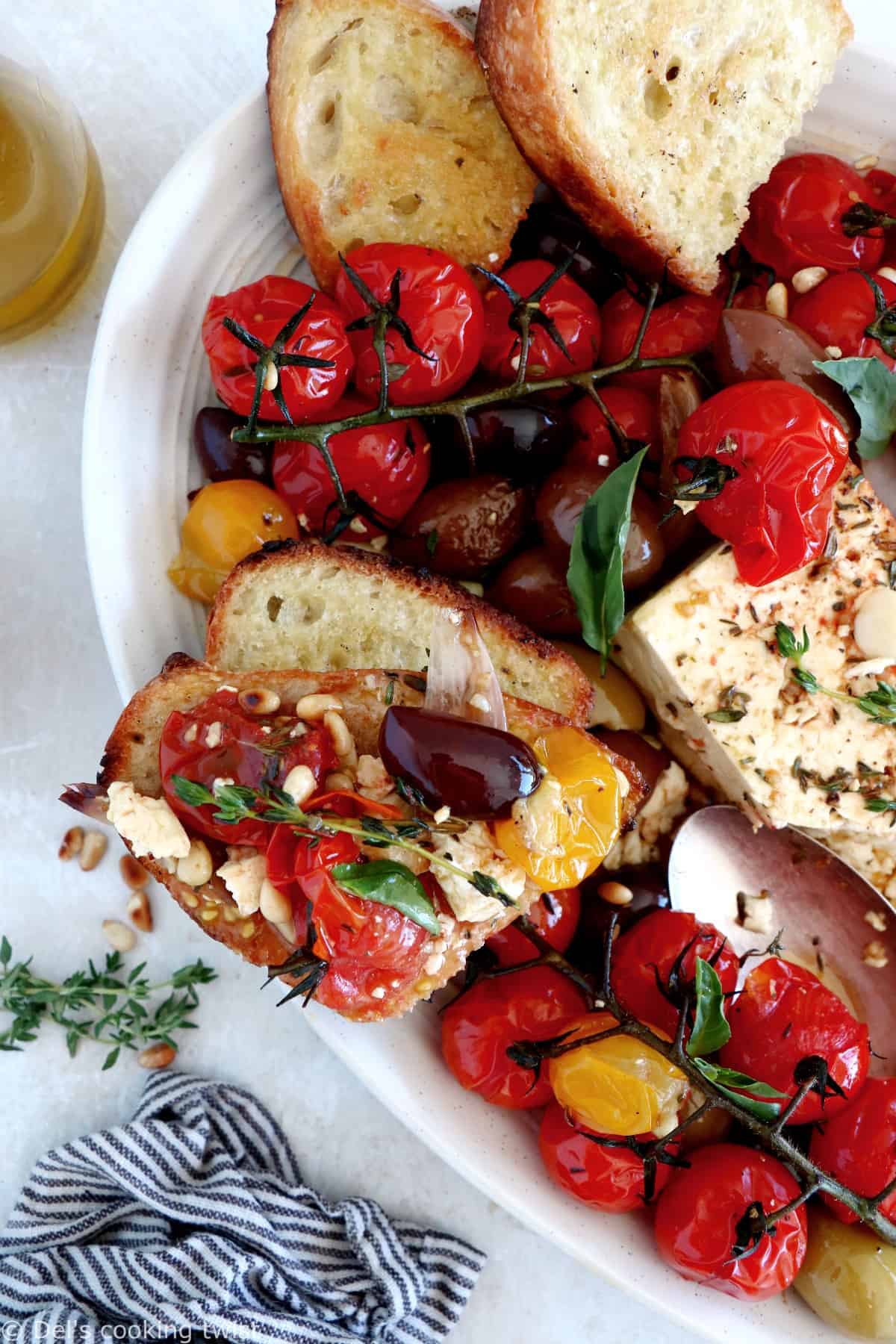 Découvrez ce plat de "baked feta", qui consiste en de la feta rôtie au four avec des tomates cerises confites et des olives marinées dans un mélange d'huile d'olive et d'herbes.