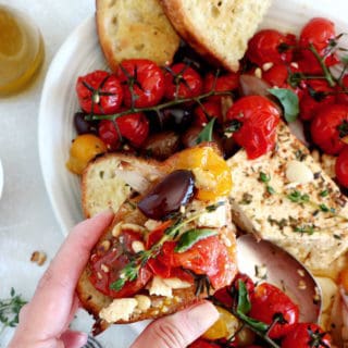 Découvrez ce plat de "baked feta", qui consiste en de la feta rôtie au four avec des tomates cerises confites et des olives marinées dans un mélange d'huile d'olive et d'herbes.