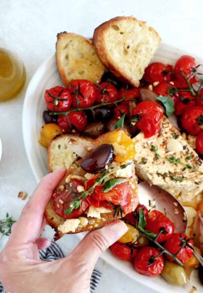 Découvrez ce plat de "baked feta", qui consiste en de la feta rôtie au four avec des tomates cerises confites et des olives marinées dans un mélange d'huile d'olive et d'herbes.