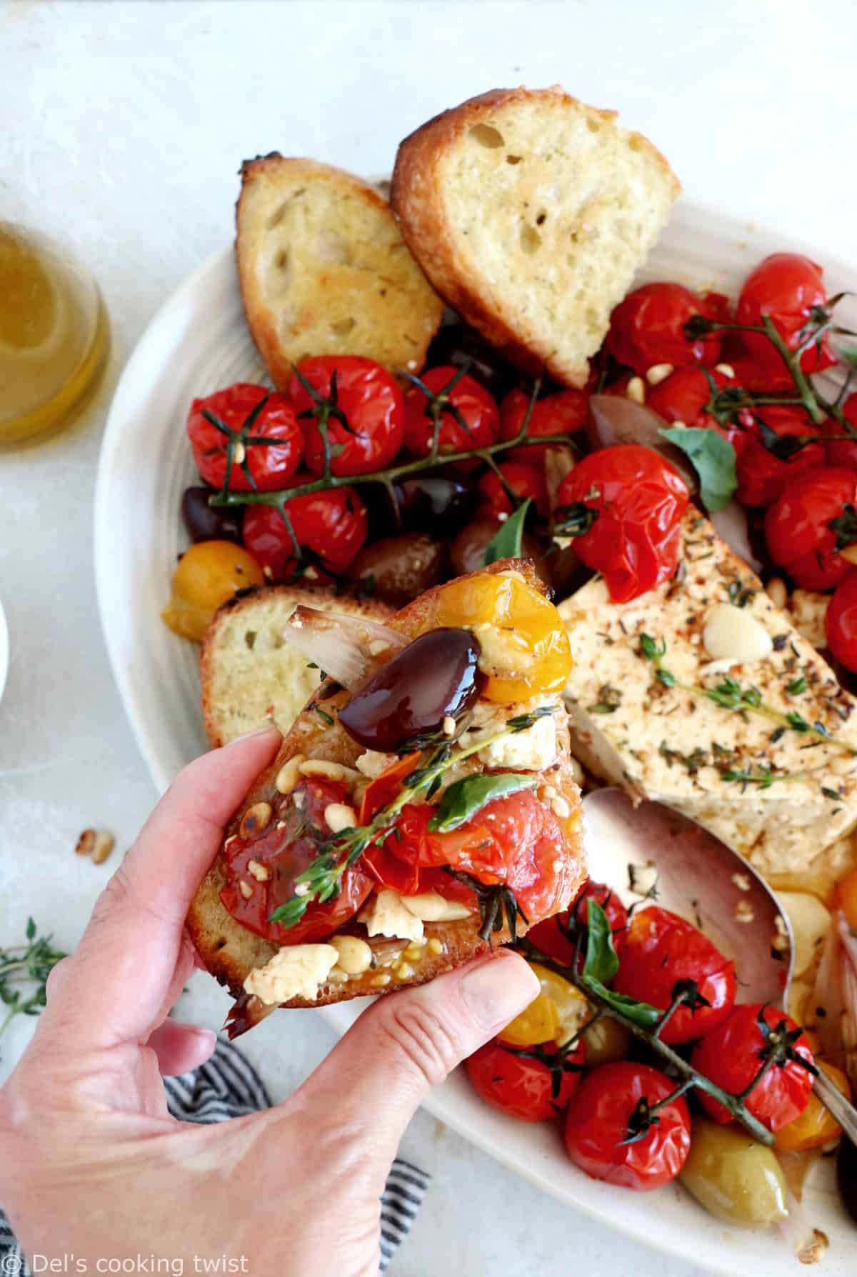 Découvrez ce plat de "baked feta", qui consiste en de la feta rôtie au four avec des tomates cerises confites et des olives marinées dans un mélange d'huile d'olive et d'herbes.