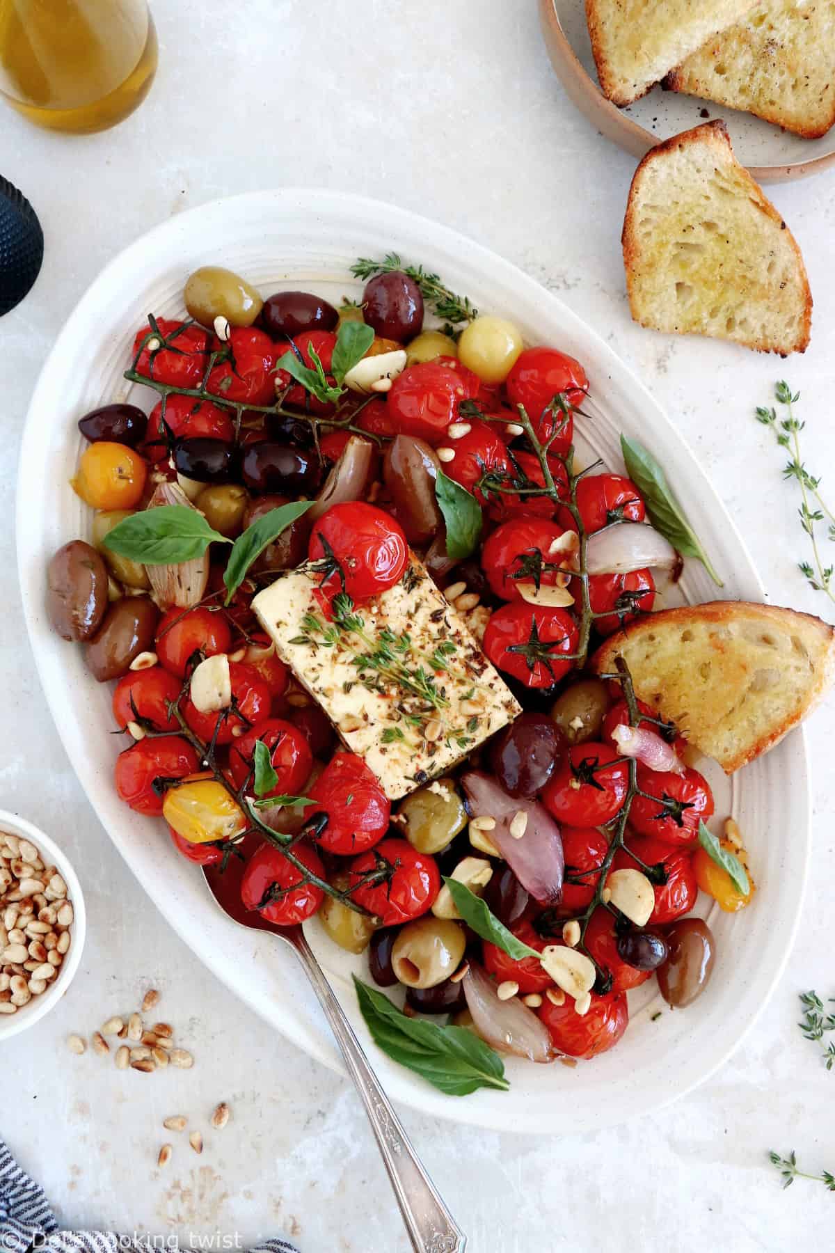 Découvrez ce plat de "baked feta", qui consiste en de la feta rôtie au four avec des tomates cerises confites et des olives marinées dans un mélange d'huile d'olive et d'herbes.