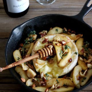 Cette recette de Brie au four aux pommes avec de l'ail rôti, du miel et un mélange d'amandes et de noisettes grillées, c'est le paradis pour les amoureux de fromages.