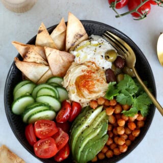 This Mediterranean mezze bowl combines a variety of hummus, tzatziki, roasted chickpeas, fresh and pickled veggies, served with pita bread.