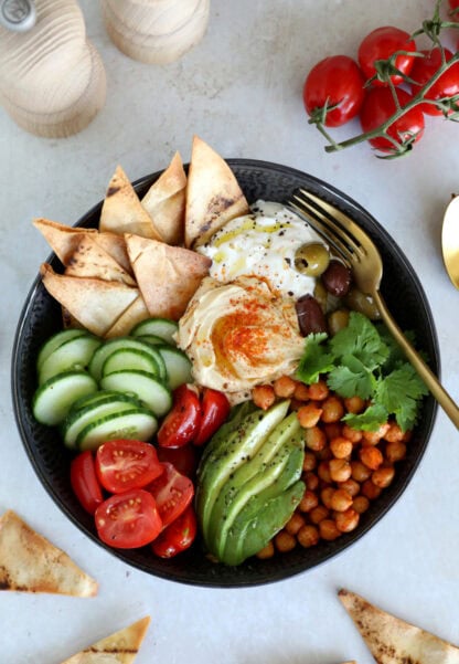 This Mediterranean mezze bowl combines a variety of hummus, tzatziki, roasted chickpeas, fresh and pickled veggies, served with pita bread.
