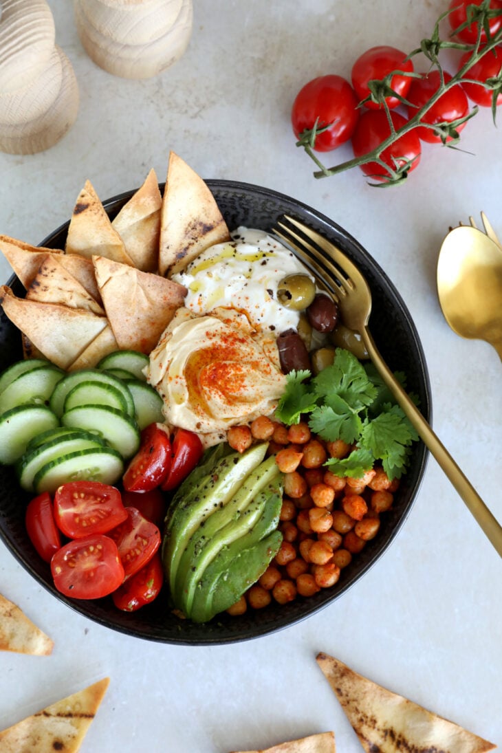 This Mediterranean mezze bowl combines a variety of hummus, tzatziki, roasted chickpeas, fresh and pickled veggies, served with pita bread.