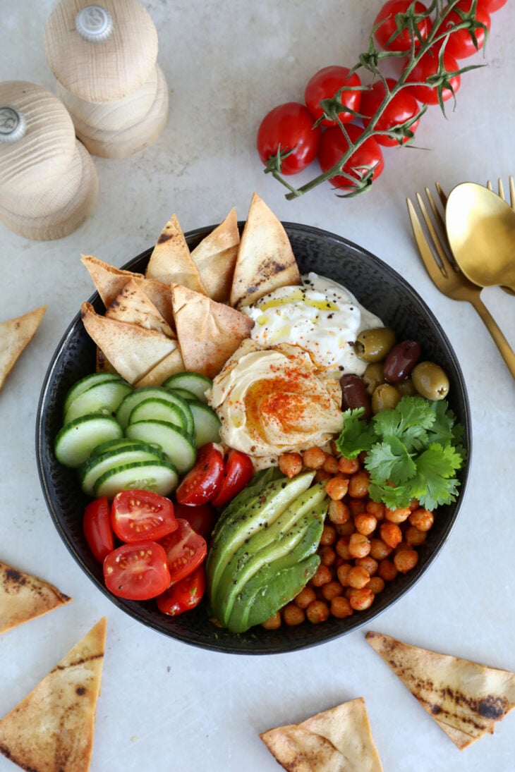 This Mediterranean mezze bowl combines a variety of hummus, tzatziki, roasted chickpeas, fresh and pickled veggies, served with pita bread.