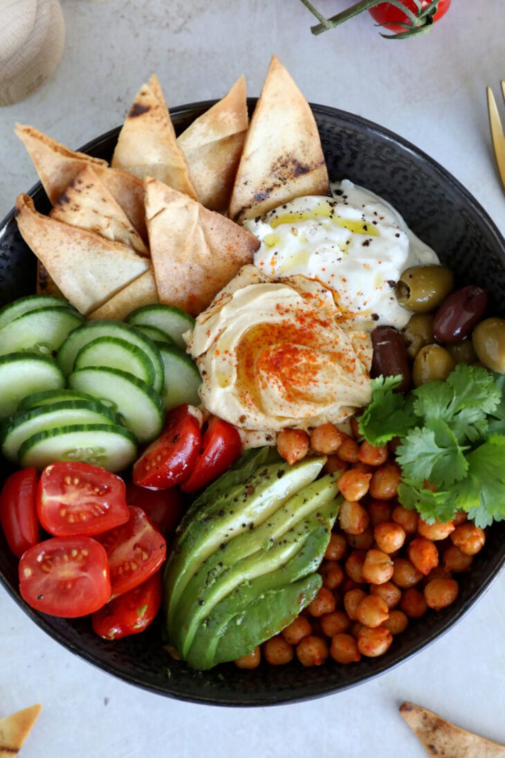 This Mediterranean mezze bowl combines a variety of hummus, tzatziki, roasted chickpeas, fresh and pickled veggies, served with pita bread.