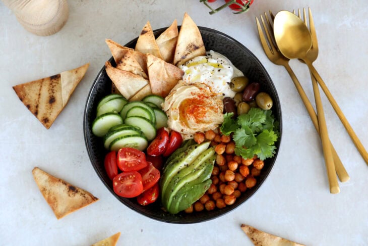 This Mediterranean mezze bowl combines a variety of hummus, tzatziki, roasted chickpeas, fresh and pickled veggies, served with pita bread.